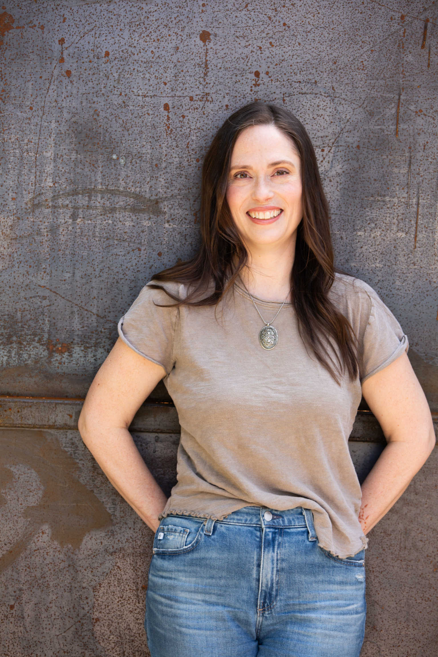 Woman wearing a beige t-shirt and blue jeans standing against a textured wall.