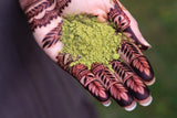 A hand with dark henna designs holding organic henna powder
