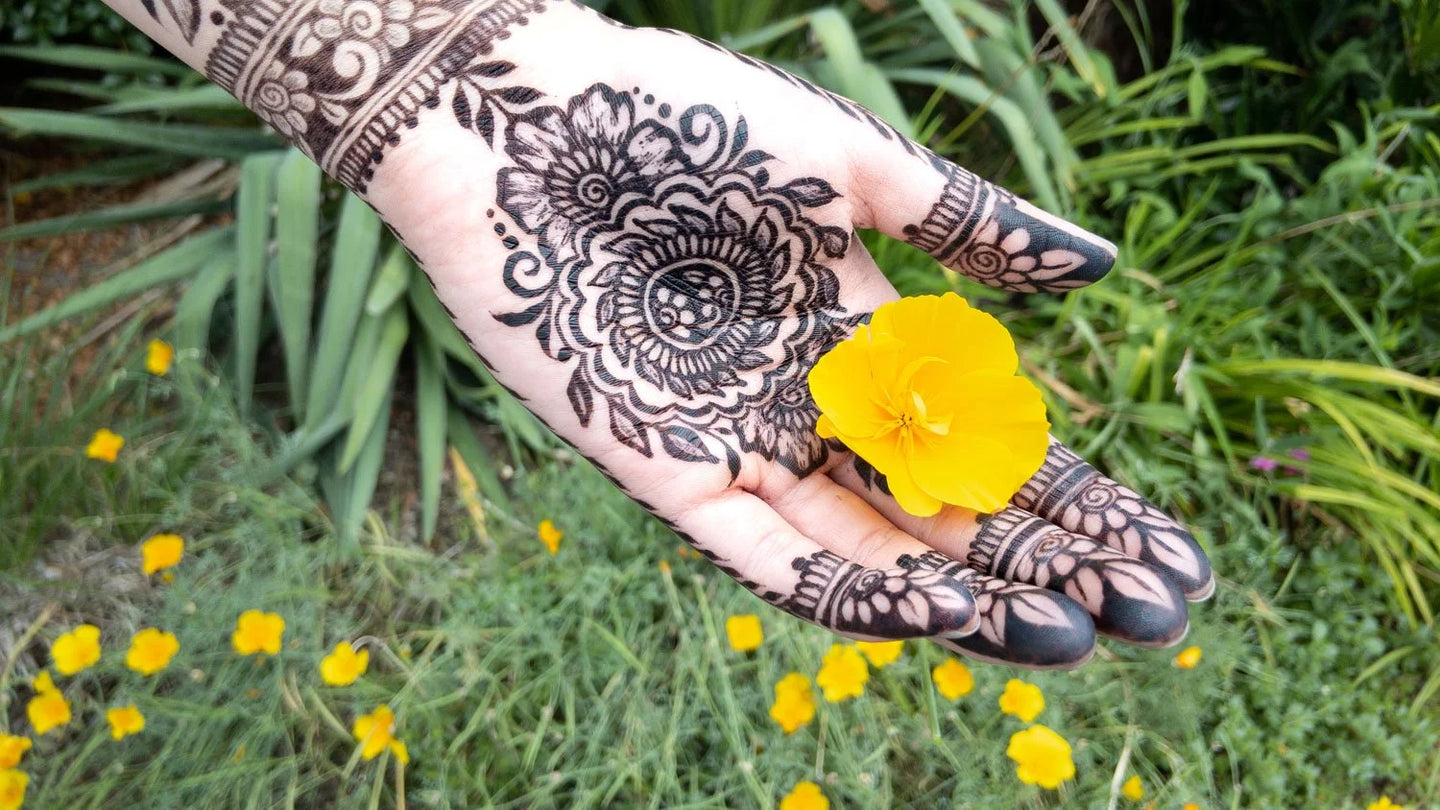 An ultra dark jagua henna stain on the palm of a hand holding a yellow flower