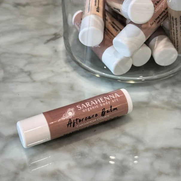 A single henna aftercare balm on a marble table next to a jar full of balms