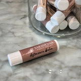 A single henna aftercare balm on a marble table next to a jar full of balms