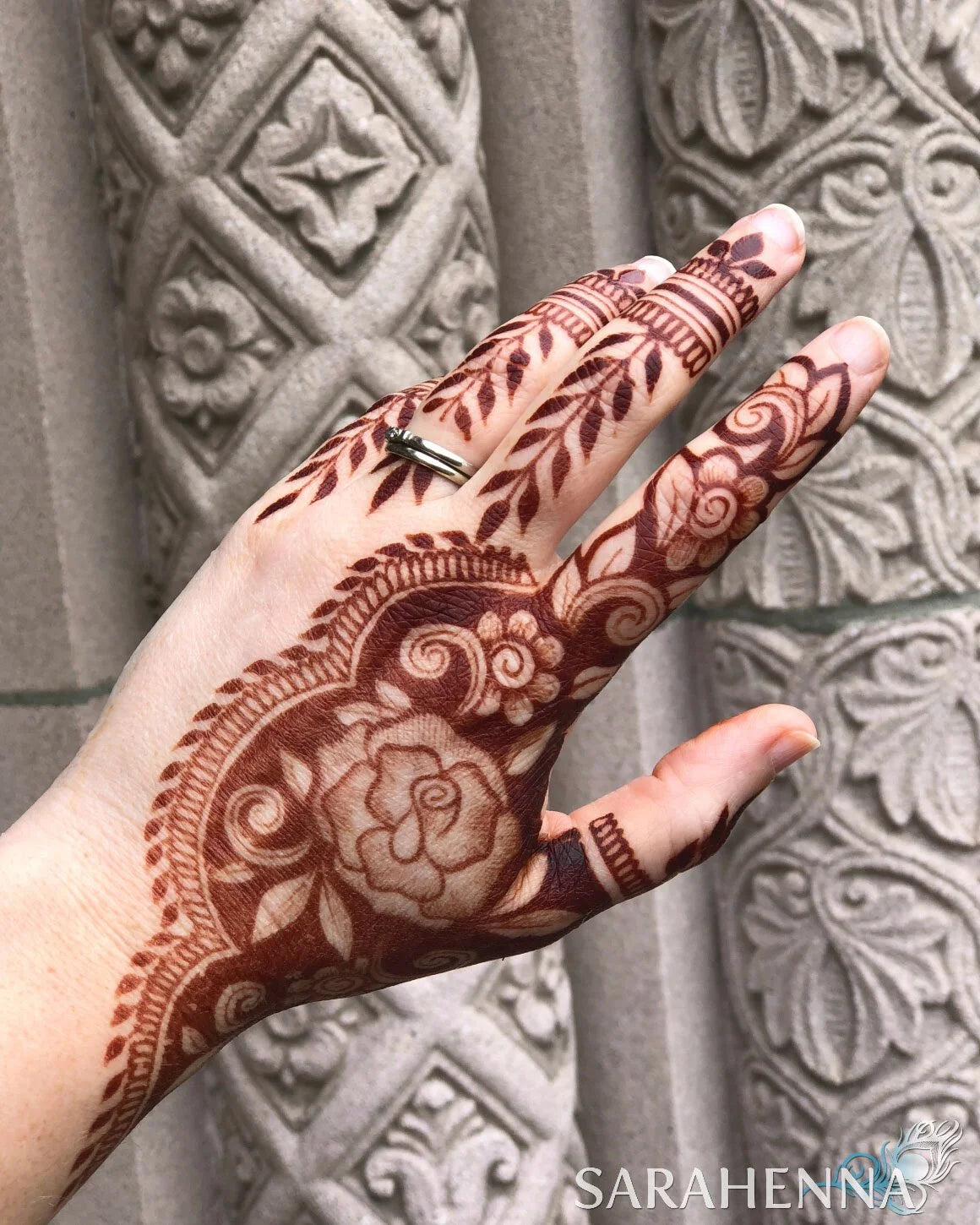 A deep burgundy henna stain on a hand in front of a stone wall