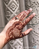 A deep burgundy henna stain on a hand in front of a stone wall