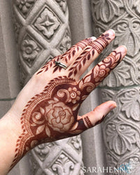 A deep burgundy henna stain on a hand in front of a stone wall