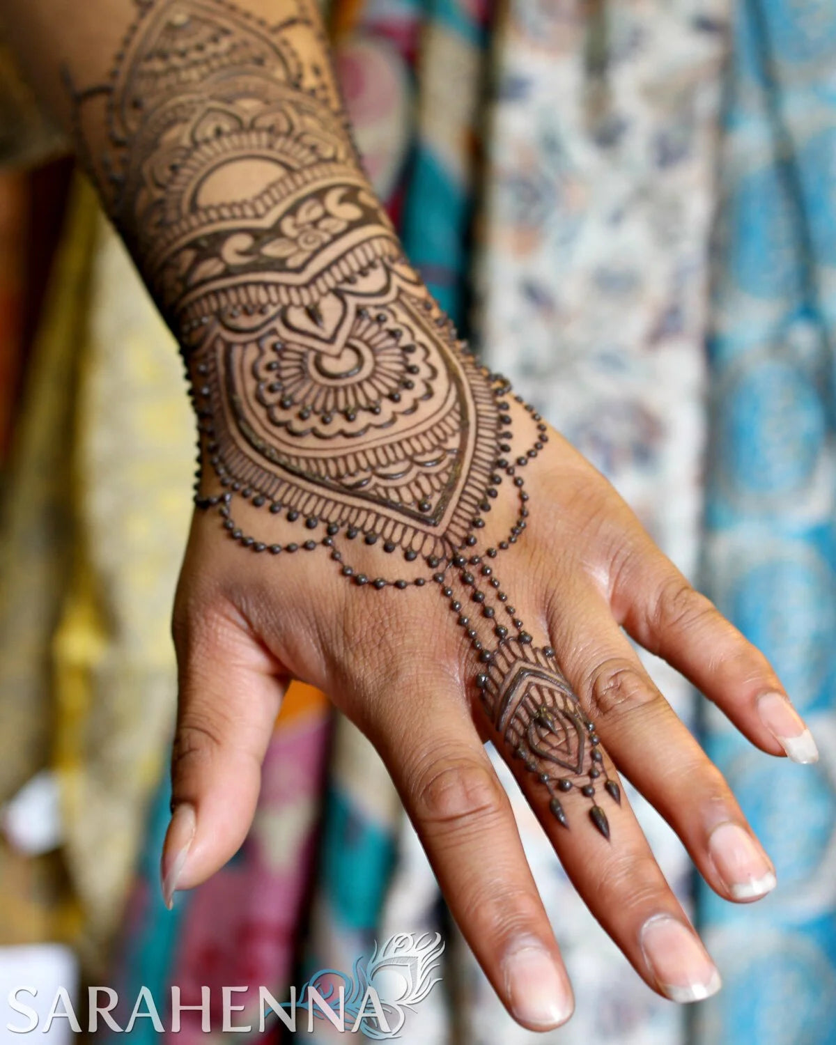 An intricate henna design on a hand with a colorful fabric background