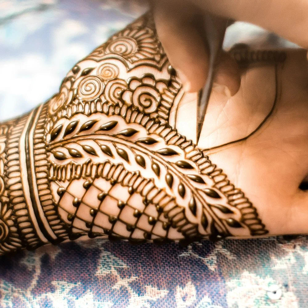 An intricate henna design being applied to a hand with a henna cone