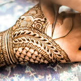 An intricate henna design being applied to a hand with a henna cone