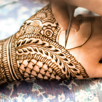 An intricate henna design being applied to a hand with a henna cone