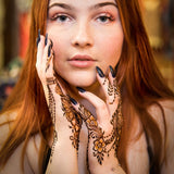 Intricate henna designs on hands that have been sprayed with finishing spray on a red haired woman