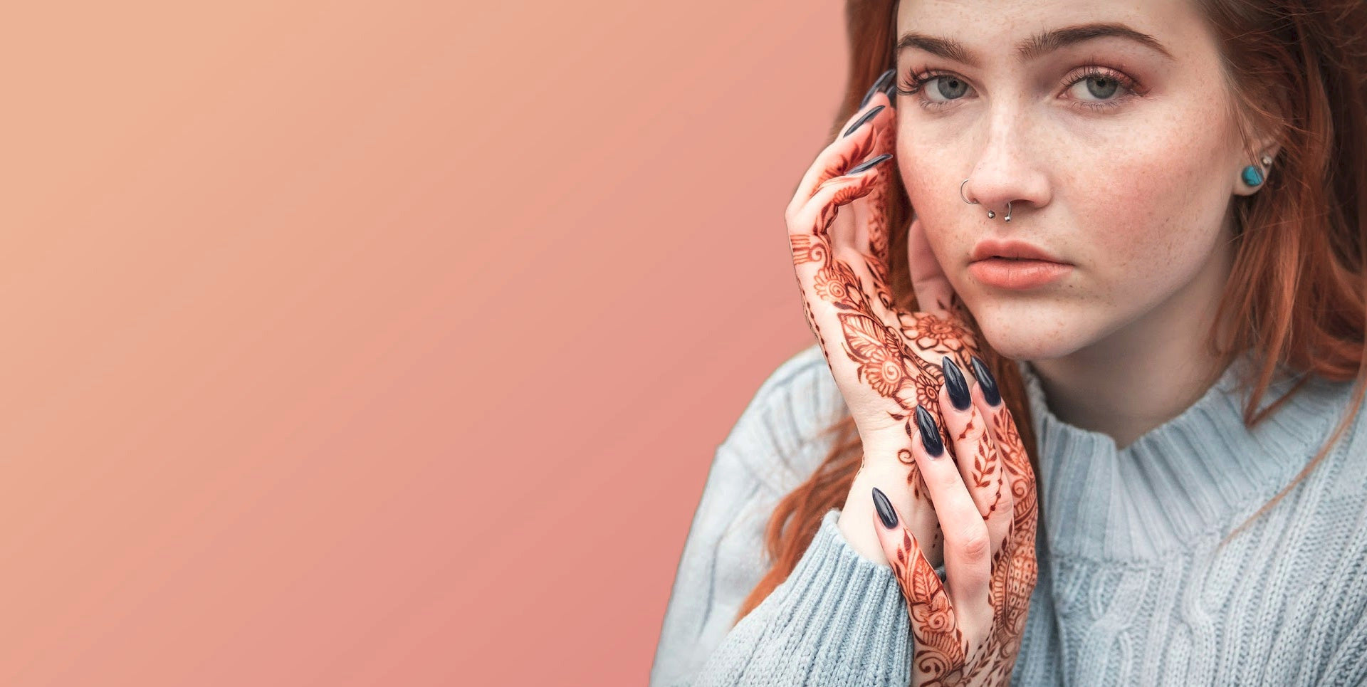 Woman with red hair and henna design on her hands against a pink background