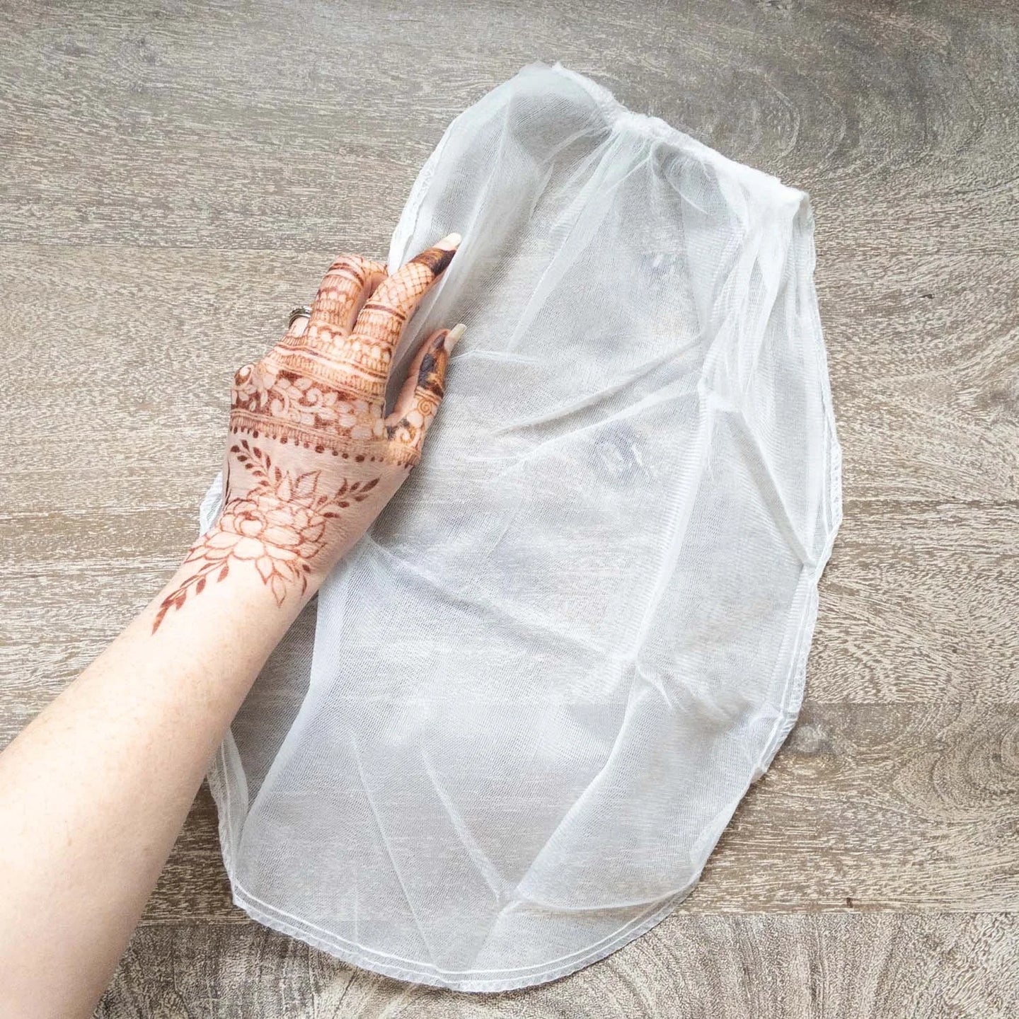 A mesh bag used for straining freshly mixed henna paste, with a henna stained hand next to it