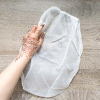 A mesh bag used for straining freshly mixed henna paste, with a henna stained hand next to it