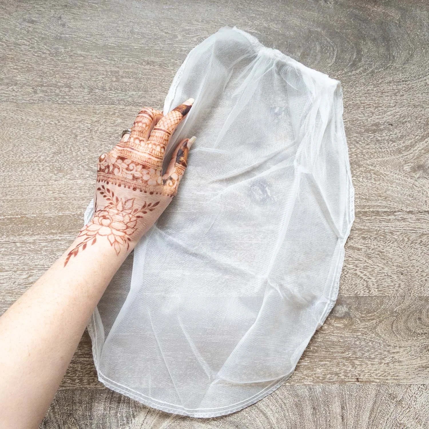 A mesh bag used for straining freshly mixed henna paste, with a henna stained hand next to it