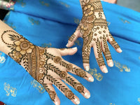 Two hands with intricate henna designs over a blue fabric