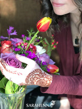 A dark henna stain on a woman's hand as she is holding and smelling flowers
