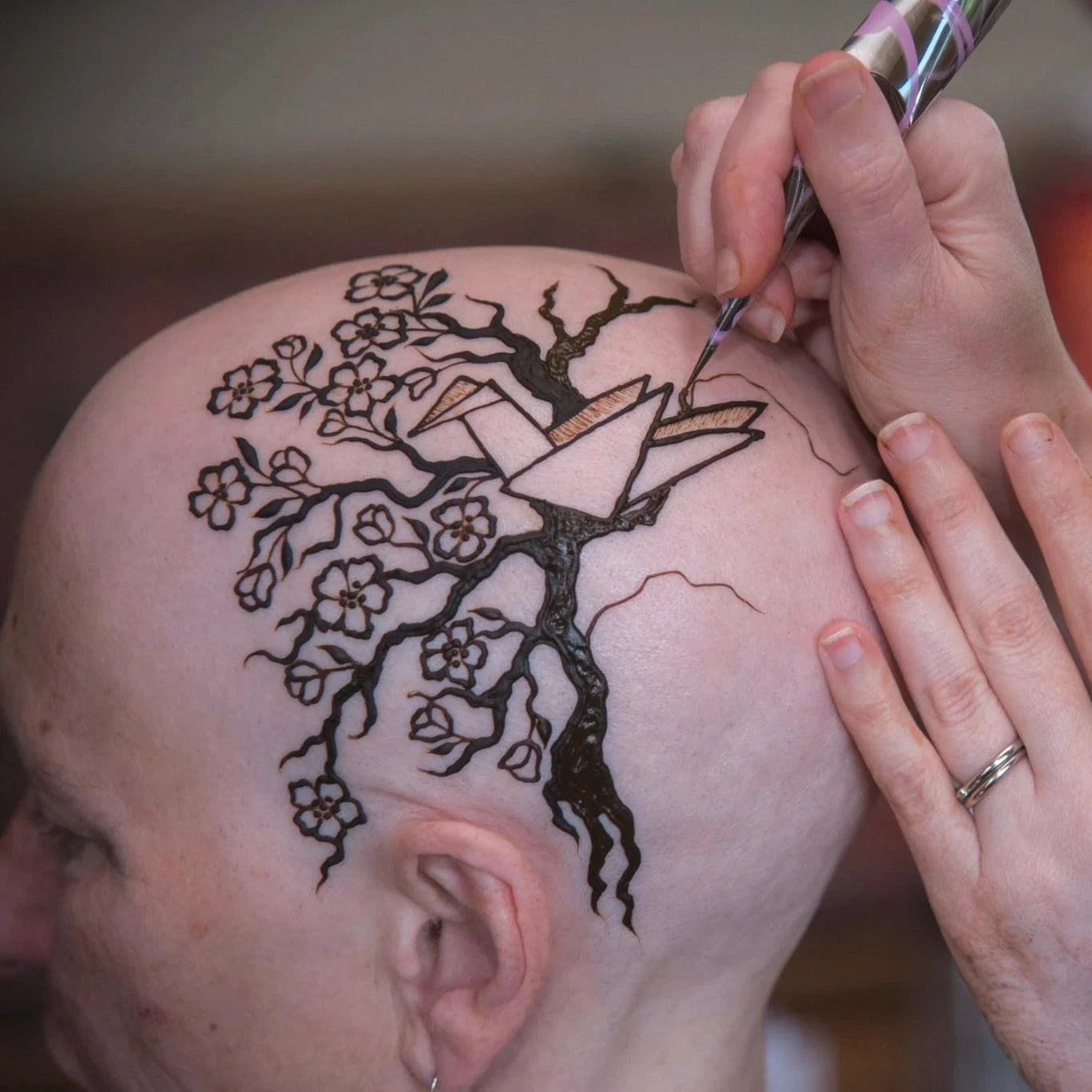 A henna crown being applied to a woman's bald head