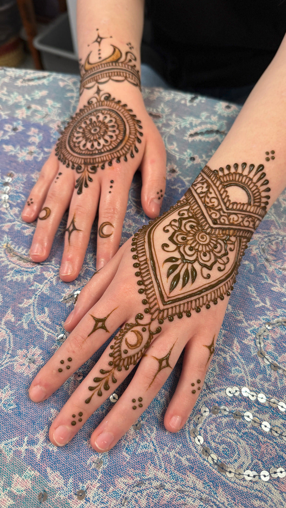 Celestial moon theme henna designs on hands against a patterned fabric background